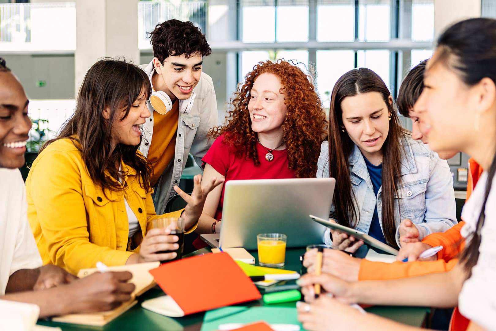 Group of college people studying together on cafeteria table at campus. Millennial student men and women working together using laptop and digital devices. Education lifestyle concept
